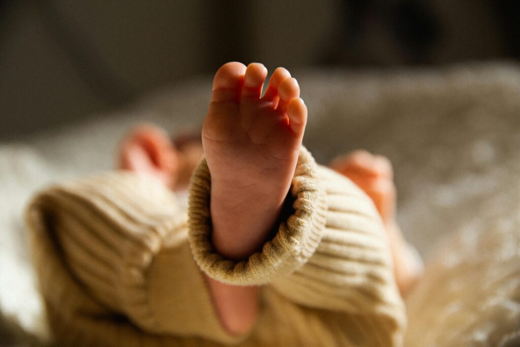 Baby liegt auf dem Rücken mit hochgestreckten Füßen auf einer Decke