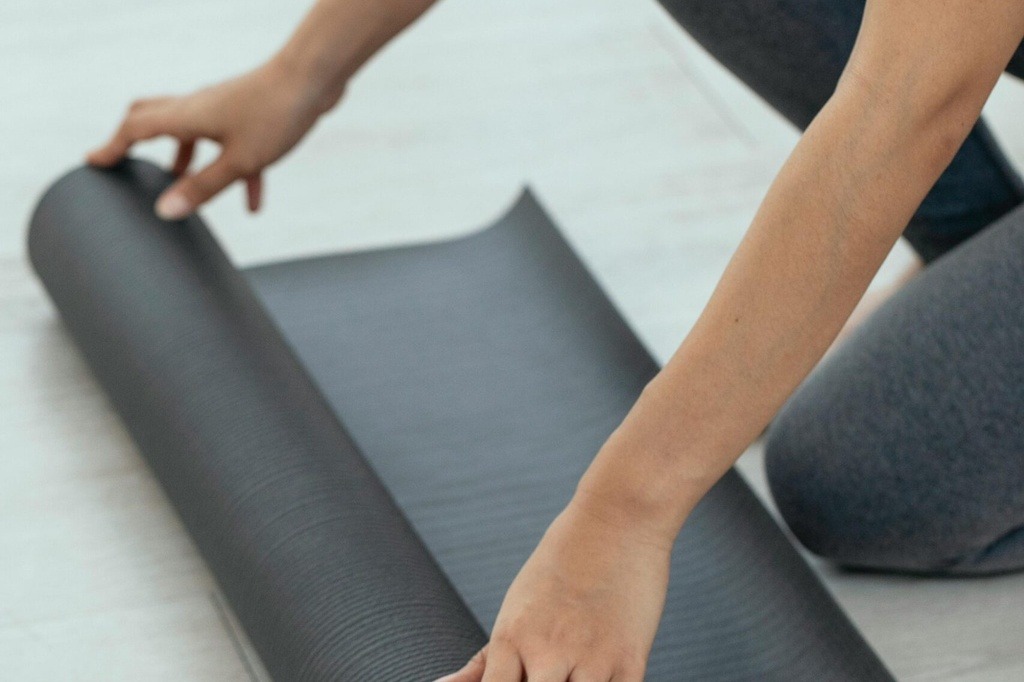 Frau rollt eine Yogamatte im Kursraum aus – Symbol für Entspannung und Rückbildung